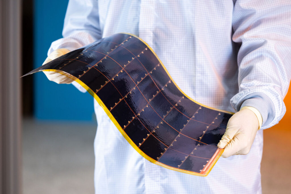 person in a lab coat wearing gloves holding a flexible solar power module