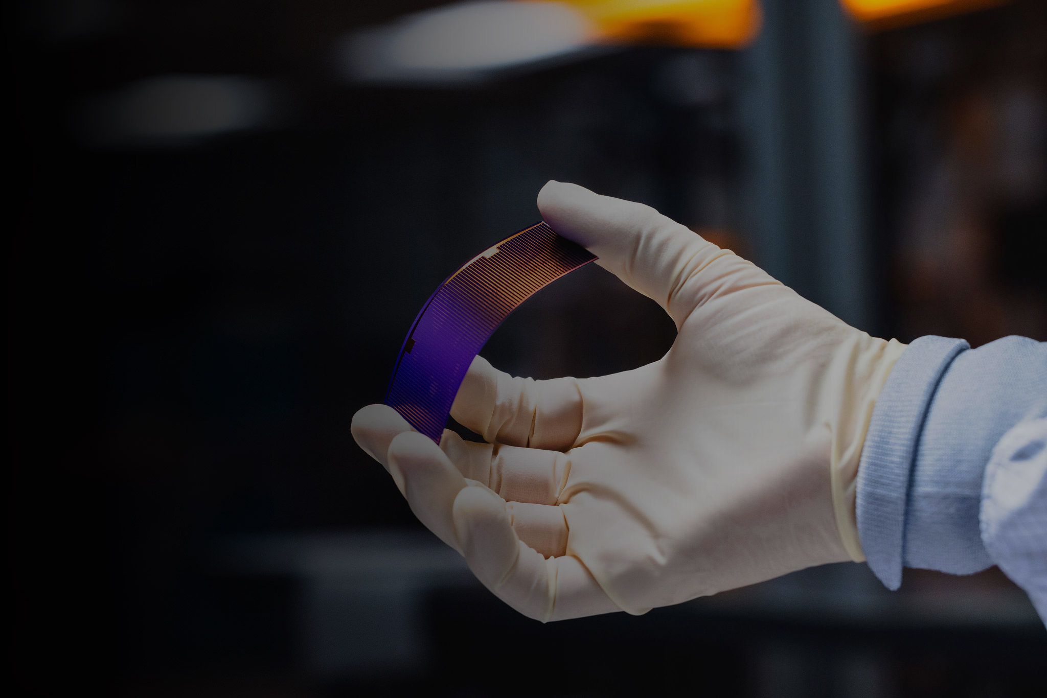 A single solar cell, helded by a gloved hand, and flexed to demonstrate it's flexibility.
