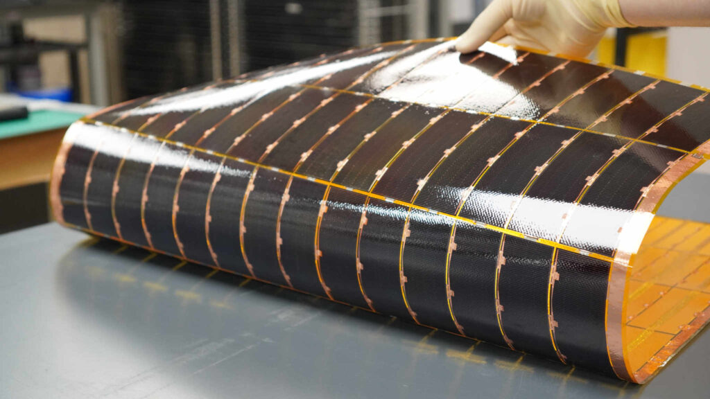 A technician wearing a white glove bends a flexible solar power module, manufactured by Solestial